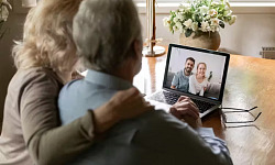 A caregiver sitting at a desk, looking at a laptop while holding a phone, symbolizing the challenges of coordinating care remotely from a long distance.