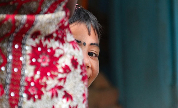 a young East-Indian girl, with a bindi dot or kala tikka on her forehead, and she is peeking out from behind something in a game of hide-and-seek