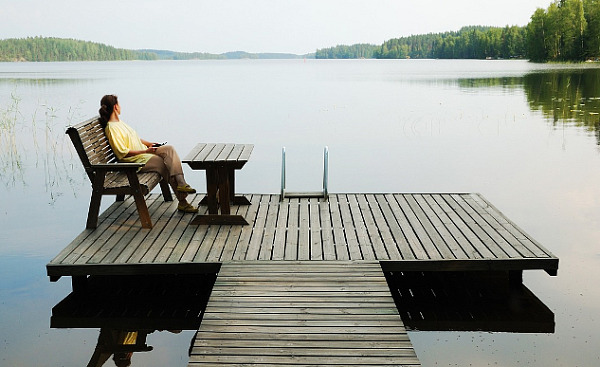 woman sitting on a bench on a platform dock surrounded by a very calm lake