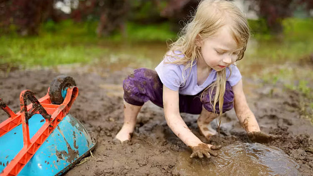 A joyful outdoor scene of children playing in a muddy garden area, hands covered in dirt, with smiles on their faces.