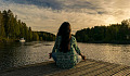 woman, seen from the back, sitting in a lotus pose on a dock by a lake