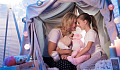 mother and daughter sitting happily in a "fort" made from sheets