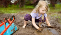 A joyful outdoor scene of children playing in a muddy garden area, hands covered in dirt, with smiles on their faces.