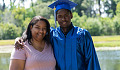 a young black man, wearing his graduation cap and robe, has his arm around his smiling mother's shoulders